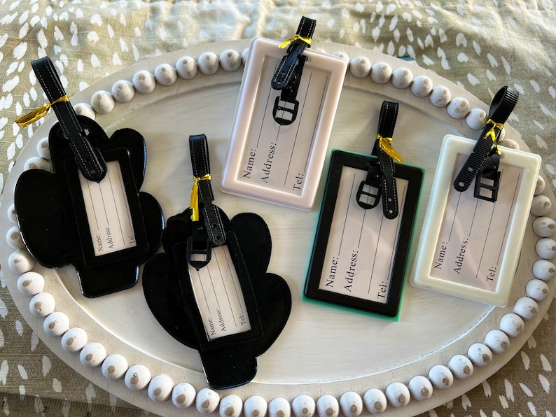 K&ouml;nnte beinhalten: F&uuml;nf Gep&auml;ckanh&auml;nger in verschiedenen Farben und Designs. Die Anh&auml;nger haben einen Platz zum Aufschreiben von Name, Adresse und Telefonnummer. Die Anh&auml;nger sind aus Kunststoff und haben ein schwarzes Band.