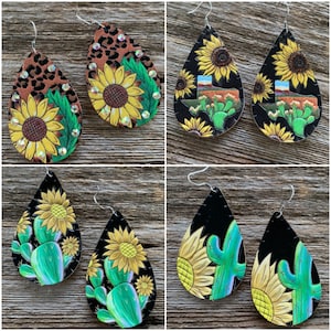 May include: A set of four pairs of dangle earrings featuring a teardrop shape. The earrings are made of leather and feature different designs, including a sunflower with cactus, a sunflower with a Texas outline, and a leopard print with a sunflower.