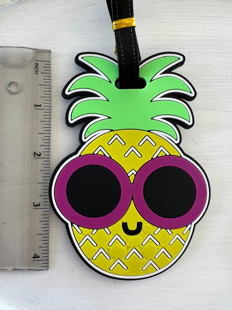 Op de afbeelding: Een gele ananas met een groene bovenkant en roze zonnebril. De ananas heeft een wit en geel patroon en een glimlachend gezicht.