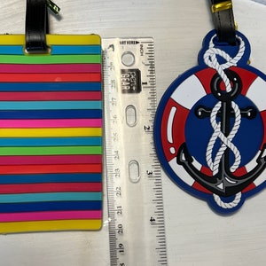 May include: Two colourful luggage tags. One tag is a rainbow striped design. The other tag is a blue and red life preserver with a black anchor and white rope.