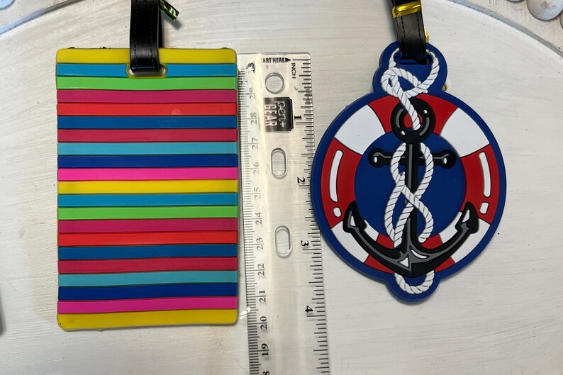 May include: Two colourful luggage tags. One tag is a rainbow striped design. The other tag is a blue and red life preserver with a black anchor and white rope.