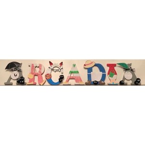 K&ouml;nnte beinhalten: Ein h&ouml;lzernes Namensschild mit der Aufschrift "ARCADIA" in bunten Buchstaben und Figuren aus dem Animationsfilm "Mein Nachbar Totoro".