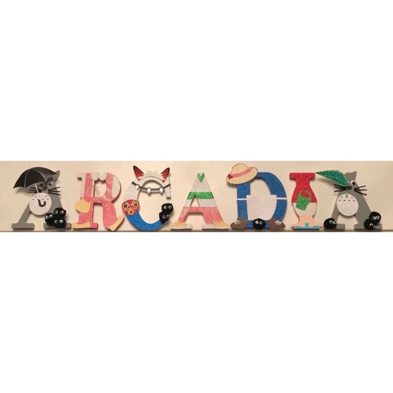 K&ouml;nnte beinhalten: Ein h&ouml;lzernes Namensschild mit der Aufschrift "ARCADIA" in bunten Buchstaben und Figuren aus dem Animationsfilm "Mein Nachbar Totoro".