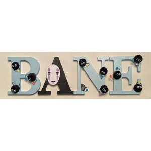 K&ouml;nnte beinhalten: Hellblaue Holzbuchstaben, die "BANE" buchstabieren, mit schwarzen Filz-Akzenten. Jeder Buchstabe hat kleine schwarze, flauschige Kugeln mit schillernden blauen, gr&uuml;nen und violetten Akzenten.