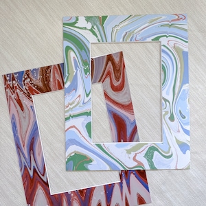 May include: Two decorative picture frames with a marbled design. The frame on top is blue, green, and white. The frame on the bottom is red, brown, and white.