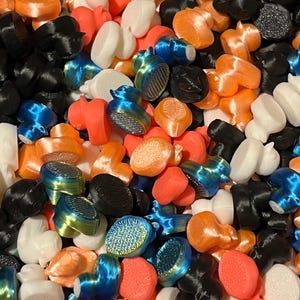 May include: A collection of colorful, 3D-printed objects in various shapes. The assortment includes pieces in black, white, orange, red, and blue. Some pieces have a textured, iridescent finish, while others are smooth.