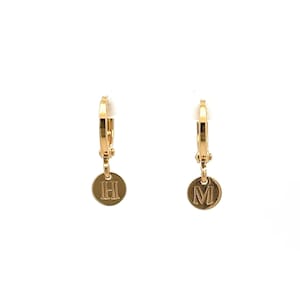 May include: A pair of gold hoop earrings with small round charms hanging from them. The charms are engraved with the letters "H" and "M".
