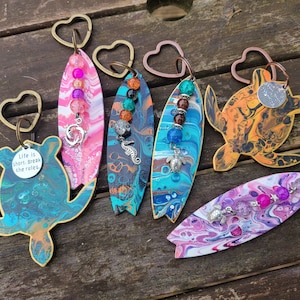 May include: A set of six colorful surfboard and turtle keychains with various charms and beads. The keychains are made of wood and painted with a marbled design. The charms include a seahorse, a turtle, and a dolphin. The beads are made of glass and come in a variety of colors. The keychains are perfect for adding a touch of whimsy to your keys or bag.