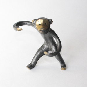 Peut inclure: Une figurine de singe en métal noir avec un visage et des bras dorés. Le singe est debout sur ses quatre pattes, les bras levés en l'air.