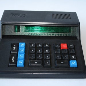 Peut inclure: Une calculatrice noire avec un écran numérique vert et un pavé numérique avec des boutons bleus et rouges. La calculatrice a des lettres cyrilliques sur les boutons.