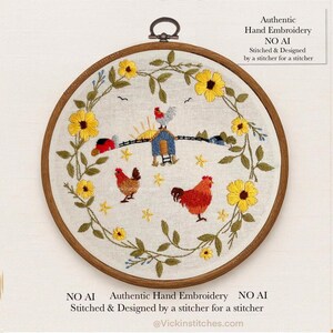 May include: A circular wooden embroidery hoop containing a white fabric panel with hand-stitched designs. The embroidery features a wreath of yellow sunflowers and green leaves surrounding two red chickens and a small blue coop with a rooster on top.