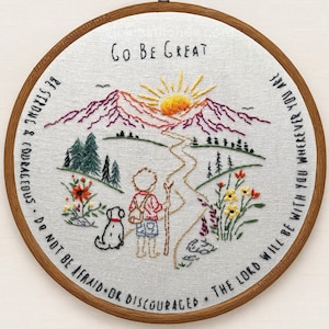 May include: Embroidered artwork in a wooden hoop. The design features a person with a dog walking a path towards a mountain range with a rising sun. Text includes "Go Be Great" and inspirational quotes.