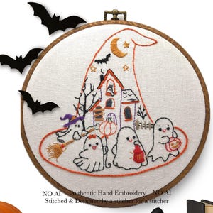 May include: Hand-embroidered Halloween-themed hoop art. The design features a witch's hat with a haunted house, ghosts, and bats. The embroidery is in orange, purple, and black on a white background, framed in a wooden hoop. The text reads "NO AI Authentic Hand Embroidery".