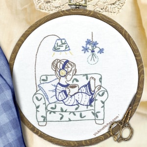 May include: Embroidered hoop art depicting a person in a striped shirt sitting in a chair with a cup of coffee, listening to music with headphones. A lamp and a vase of flowers are in the background. The hoop is brown wood with a white fabric background. The text "Vickinstitches.com" is in the lower right corner.