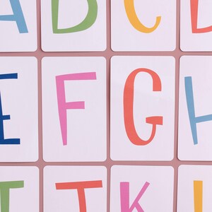 May include: A set of alphabet flashcards with colorful letters on white cards. The letters are in a playful, handwritten style. The letters A, B, C, D, E, F, G, H, I, J, K, and L are shown.