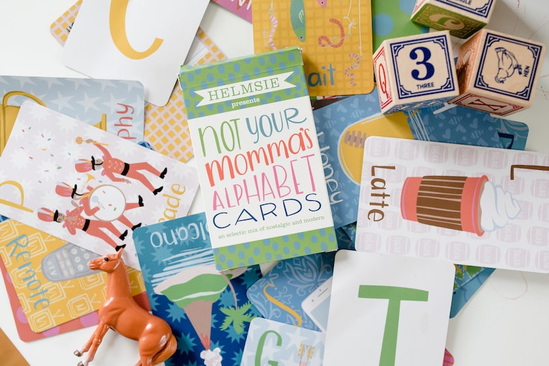 May include: A set of alphabet flash cards with a green and white box that says "Not Your Momma's Alphabet Cards: An eclectic mix of nostalgic and modern". The cards feature illustrations of a parade, a remote, a latte, and a honeybee.