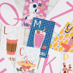 May include: A set of alphabet flash cards with colorful illustrations and pink letters. The cards feature images of a carousel, a milkshake, an astronaut, a yoga pose, a coffee cup, and a marching band.