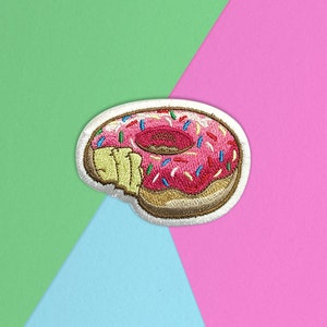 May include: An embroidered donut patch in pink and white with colourful sprinkles.