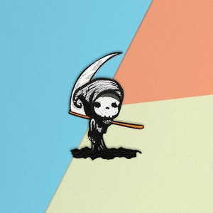 May include: Black and white embroidered patch of a cartoon grim reaper holding a scythe. The reaper is wearing a hooded robe and has a skull-like face.
