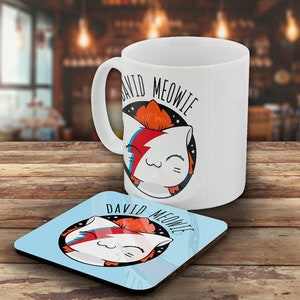 May include: White ceramic mug and matching coaster featuring a cartoon cat with a lightning bolt and star design. The mug and coaster have the words "DAVID MEOWIE" printed on them. The coaster is square and light blue.