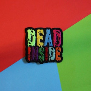 Könnte beinhalten: Ein bunter gestickter Aufnäher mit den Worten "DEAD INSIDE" in einer tropfenden Schriftart. Der Aufnäher ist schwarz mit regenbogenfarbenen Buchstaben.