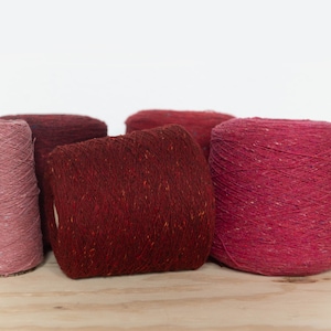 May include: Four spools of yarn in shades of pink and red. The yarn is a speckled blend of fibers.