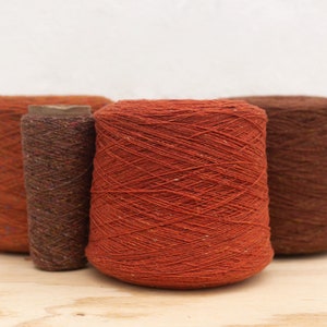 May include: Three spools of yarn in different shades of brown and orange. The yarn is textured and has a subtle sheen.