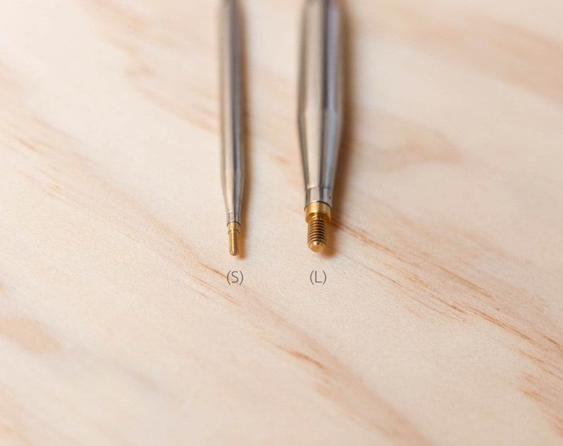 Op de afbeelding: Close-up van twee metalen breinaalden met gouden puntjes. De naalden zijn gemarkeerd met "S" en "L" voor de maat.