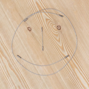 Puede incluir: Dos bridas de cable de metal plateado dispuestas en forma de cara sonriente sobre una superficie de madera marrón claro.