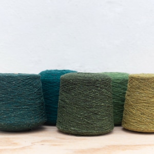 May include: Five spools of yarn in shades of green, teal, and olive. The yarn is a textured, tweed-like material.