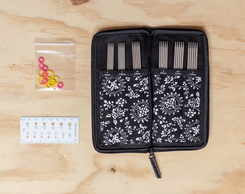 Puede incluir: Una funda negra con cremallera y un estampado floral blanco contiene un juego de 12 agujas de tejer. Las agujas est&aacute;n dispuestas en filas por tama&ntilde;o, con tama&ntilde;os de 2,25 mm, 2,5 mm, 3,0 mm, 3,25 mm, 3,5 mm y 3,75 mm. Tambi&eacute;n se muestra una bolsa de pl&aacute;stico transparente con marcadores de punto de color rosa y amarillo.