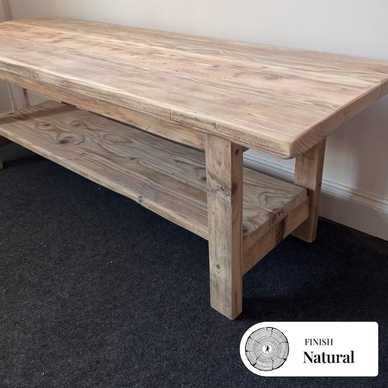 May include: A rectangular wooden coffee table with a natural light brown finish, featuring a smooth top surface and a lower shelf supported by four sturdy legs. The wood grain is visible throughout the piece, showcasing knots and natural patterns.