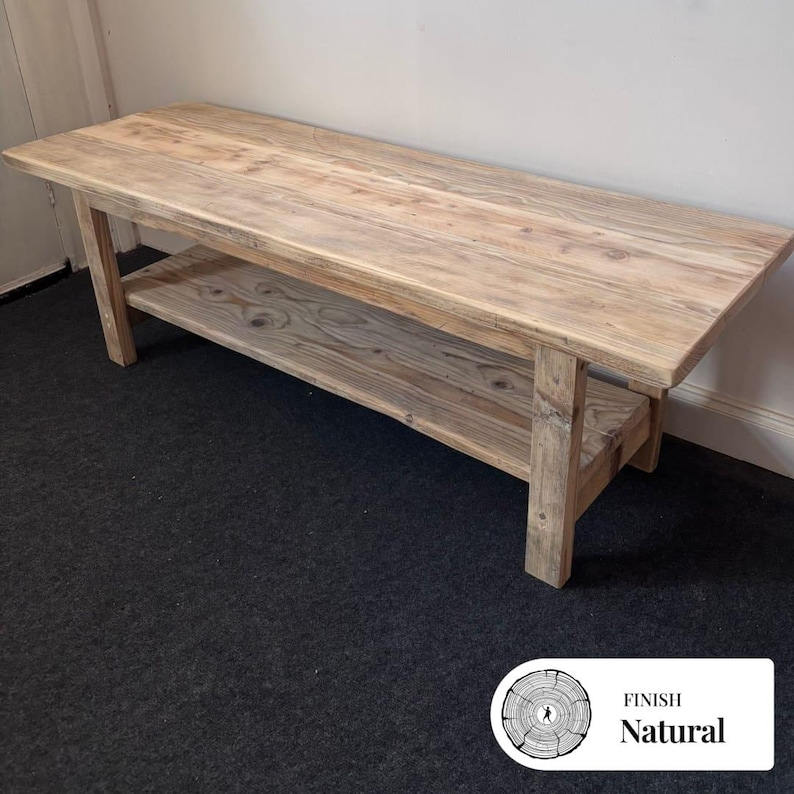 May include: A rectangular wooden bench with a natural light brown finish, featuring a flat top surface and a lower shelf supported by four sturdy legs. The wood grain is visible throughout the structure, and a small label reads FINISH Natural.