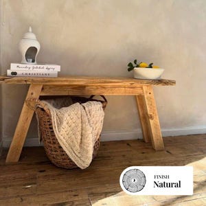 Può includere: Panca in legno rustico con finitura naturale. Un cesto intrecciato con una coperta color crema è posto sotto la panca. Un oggetto decorativo in ceramica bianca e libri sono sulla panca. Una ciotola di limoni e verdura è anche sulla panca.