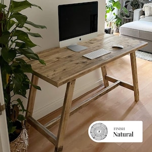 Puede incluir: Un escritorio de madera natural con un monitor de ordenador, un teclado y un ratón. El escritorio tiene una parte superior rectangular y patas anguladas. El acabado es natural. El escritorio mide aproximadamente 152 cm de largo.