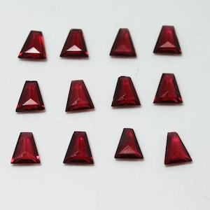 May include: Twelve red, faceted, triangular-shaped gemstones arranged in three rows of four. The gemstones are on a white background.