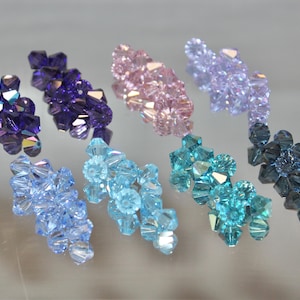 May include: Assortment of crystal beads in various colours, including blue, purple, pink, teal, and black. The beads are arranged in rows and are all the same size and shape.