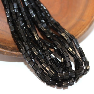 May include: A strand of black square glass beads. The beads are faceted and have a shiny finish.