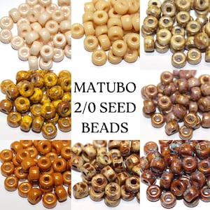 May include: Assortment of 2/0 seed beads in various colours and patterns, including solid beige, brown with gold flecks, and brown with white flecks. The beads are labelled "MATUBO 2/0 SEED BEADS".