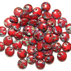 May include: A pile of red and blue ceramic beads with a speckled pattern. The beads have two holes for stringing.