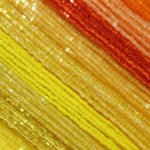 May include: A close-up of a variety of seed beads in shades of yellow, orange, and red. The beads are arranged in rows, creating a gradient effect.