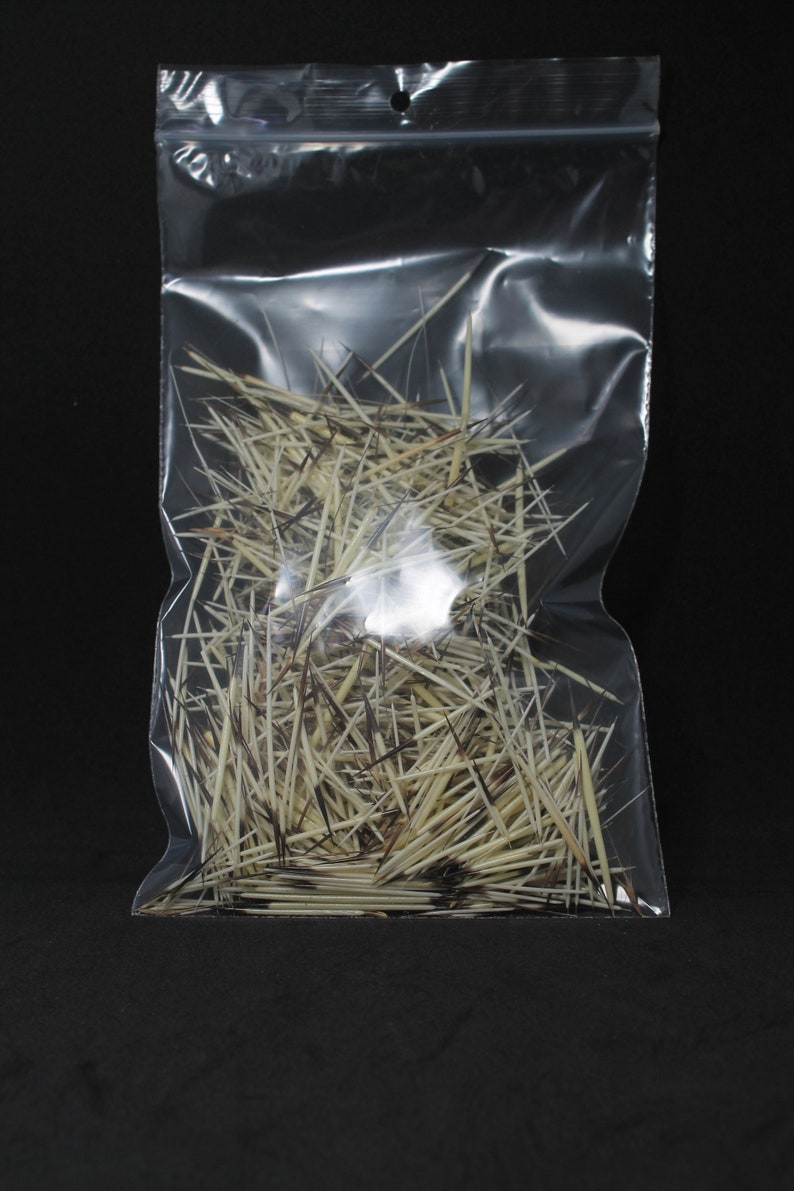 May include: A clear plastic bag filled with a large quantity of thin, light brown and white feathers. The feathers are arranged in a random, chaotic pattern.