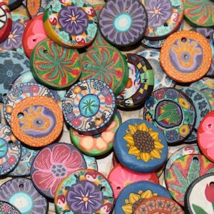May include: Assortment of colorful round wooden buttons with various designs, including flowers, peace signs, and abstract patterns. The buttons are approximately 1 inch in diameter.