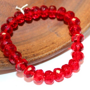 May include: A red glass bead bracelet with faceted beads. The bracelet is on a wooden surface.