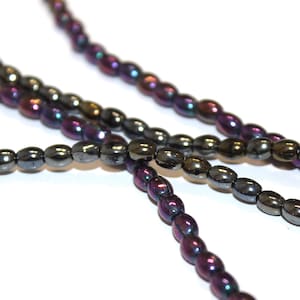 May include: Close-up of several strands of iridescent oval beads. The beads have a metallic sheen with colors ranging from purple to bronze. The beads are strung together, creating a necklace or bracelet.