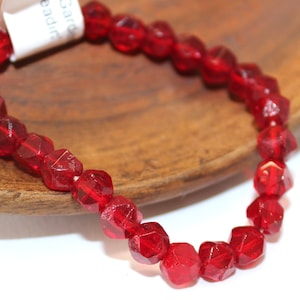 May include: A red glass bead bracelet with faceted beads. The bracelet is on a wooden surface.