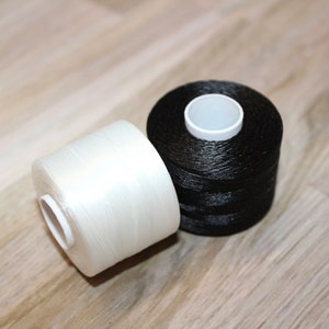 May include: Two spools of thread, one white and one black, are shown on a wooden surface.