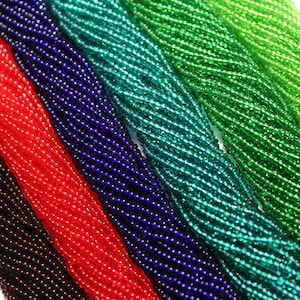 May include: A close-up of six strands of seed beads in various colours, including brown, red, blue, teal, and green. The beads are arranged in a fan shape, showcasing their iridescent sheen.