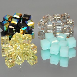 May include: An assortment of colorful cube-shaped beads. The beads are in various colors, including iridescent black, yellow, clear, and light blue. These beads are likely used for jewelry making or other crafts.