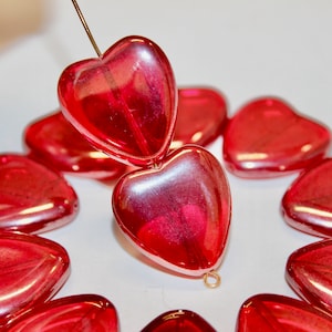 May include: A string of red heart-shaped glass beads. The beads are translucent and have a slight iridescent sheen. The beads are strung on a wire and are ready to be used in a craft project.